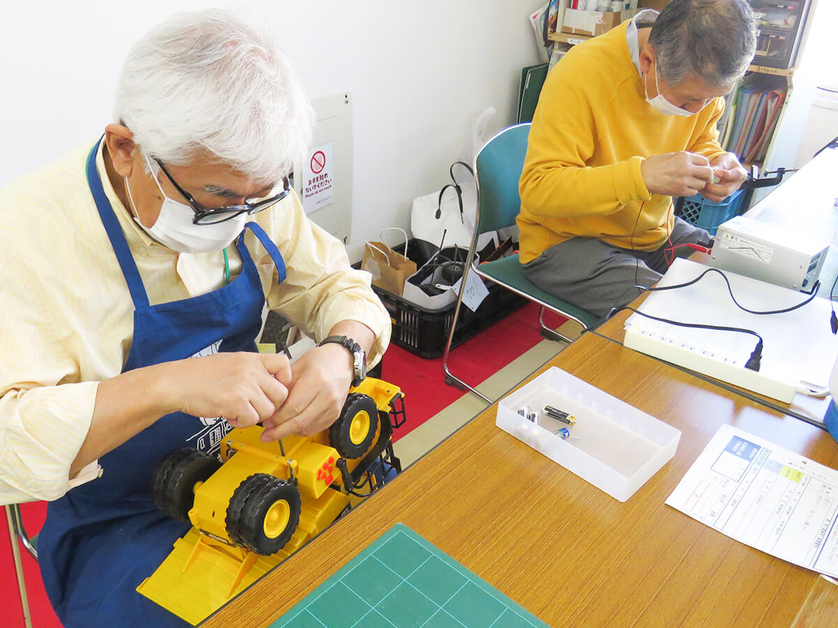 おもちゃを修理する男性2名。ドライバーなどの工具で分解しようとしている。