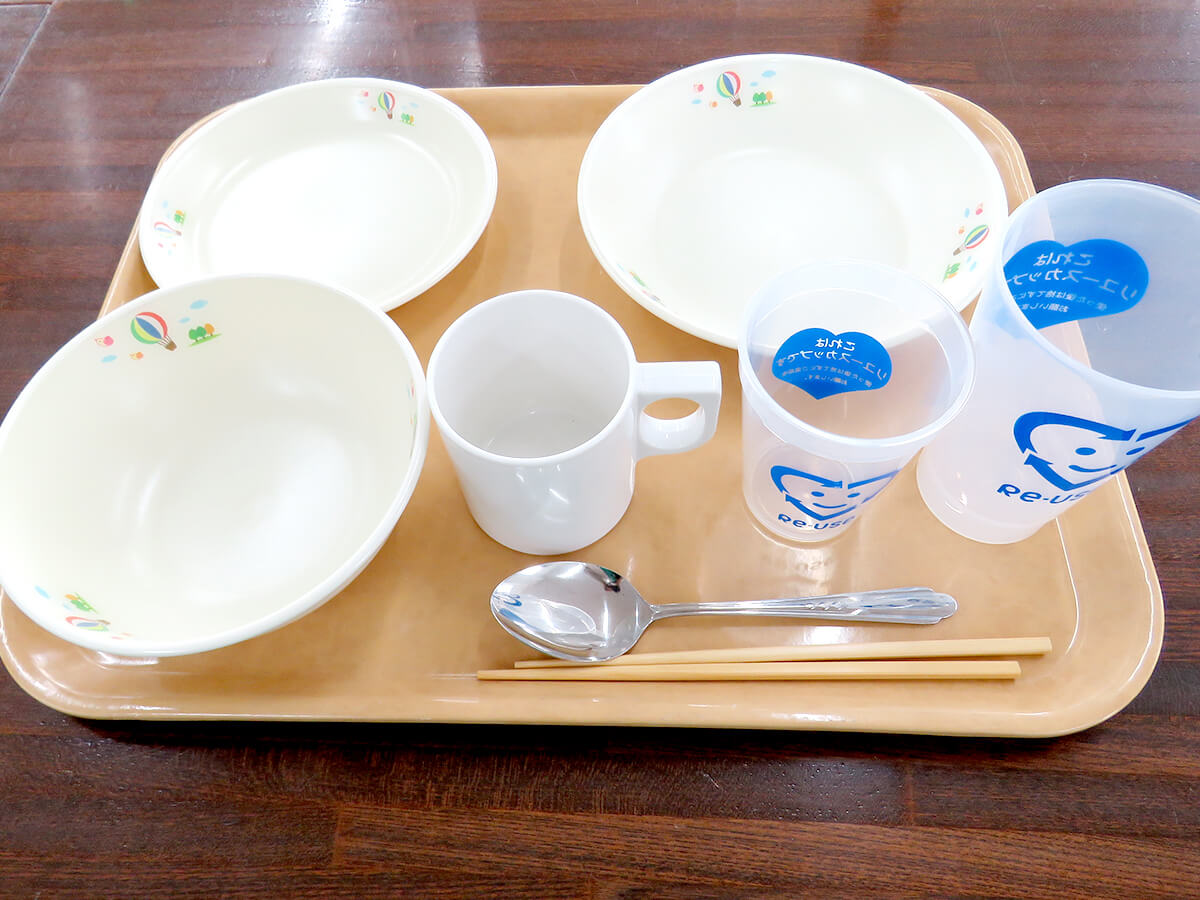 リユース食器の写真。お皿やコップ、はしやスプーンが一式トレイに乗っている。